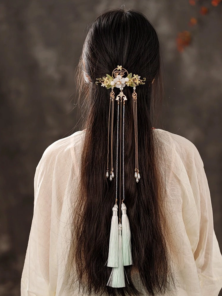 Woman wearing an elegant Chinese Hanfu back hair pin with gold floral frame, white jade-like flowers, osmanthus details, layered chain tassels, and light cyan pendants in long dark hair
