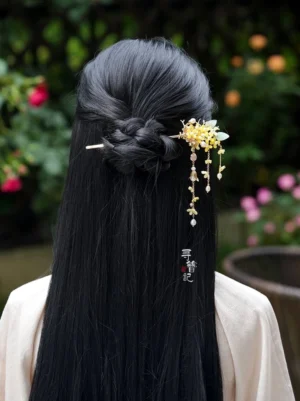 Model wearing an osmanthus pearl long tassel Hanfu hairpin in a braided half-up hairstyle outdoors with a soft floral garden background