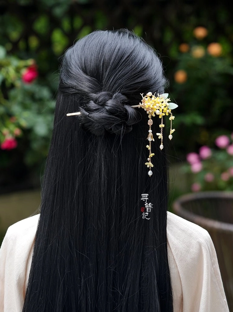 Model wearing an osmanthus pearl long tassel Hanfu hairpin in a braided half-up hairstyle outdoors with a soft floral garden background