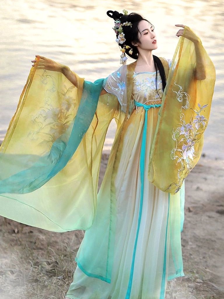 Outdoor waterside view of a Tang Dynasty Hanfu Heziqun dress with ombre yellow cyan ivory colors floral embroidery wide sleeves and fitted cyan waist sash