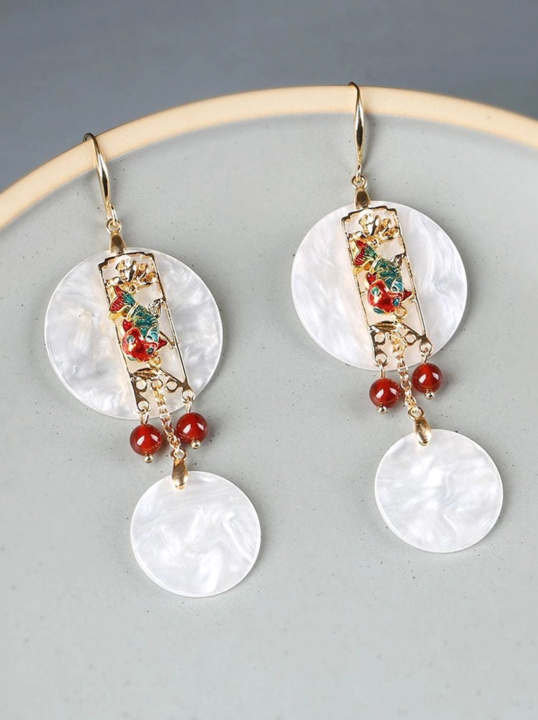 Pair of matching Chinese shell drop earrings arranged on a light gray ceramic plate showing the decorative floral pattern