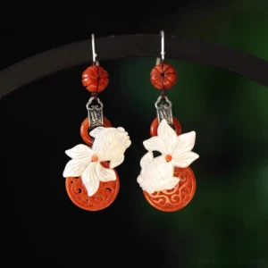 Pair of red jade koi tassel Chinese earrings displayed on a black jewelry stand, showing matching carved koi pendants, red carved beads, and silver hook closures