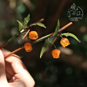 Hand holding traditional Chinese hair stick featuring three glossy orange lantern berries, green leaves, and natural bamboo texture