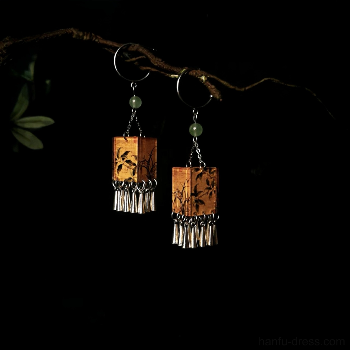 Orchid print palace lantern tassel Chinese hook earrings displayed with green foliage on dark background