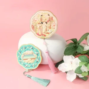 Two decorative Chinese pocket mirrors displayed with flowers, featuring turquoise crane palace artwork and pink classical court lady artwork