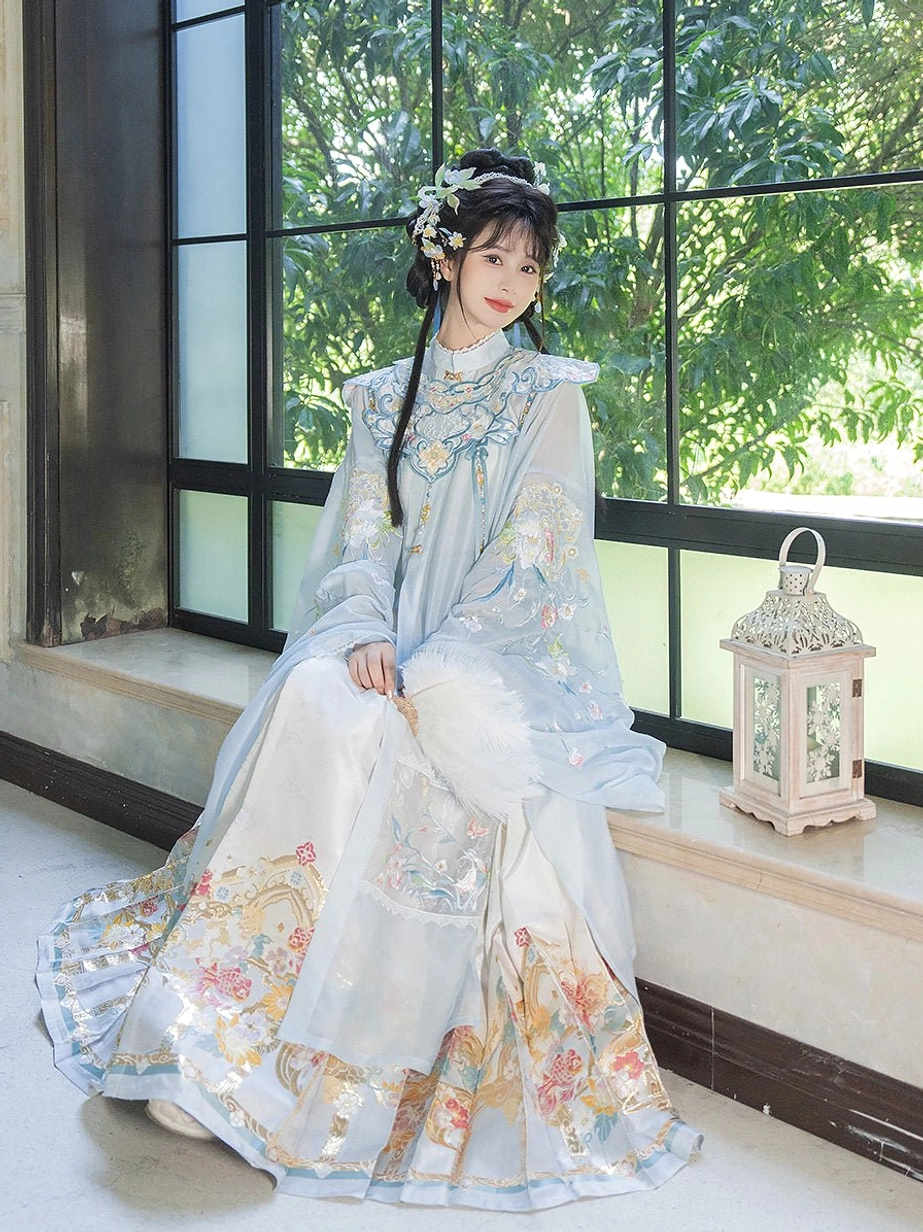 Side view of a woman in a soft pale blue Ming Dynasty hanfu robe and embroidered ivory Mamian skirt beside a sunlit window