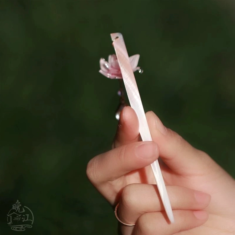 Side profile of pale pink traditional Chinese hair stick with lotus flower pendant against a soft green outdoor background