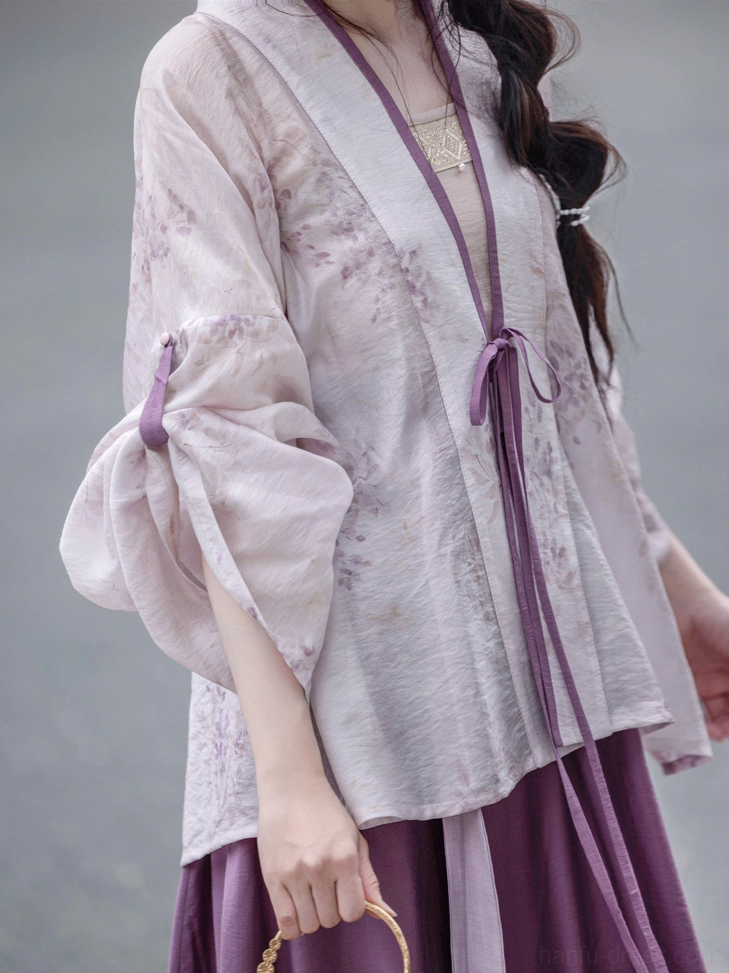 Close-up of the pale purple sheer Hanfu cardigan showing subtle wisteria floral print, crossover V-neck, dark purple drawstring ties, and bow sleeve details