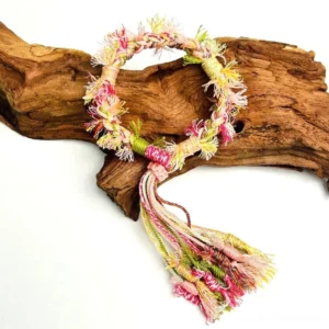 Pastel pink yellow and green handwoven Chinese bracelet with Tibetan-inspired knots and long multicolour tassel displayed on driftwood