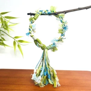 Pastel handwoven Tibetan-inspired knot tassel bracelet hanging from a wooden twig with braided mixed-color cords and long fringe