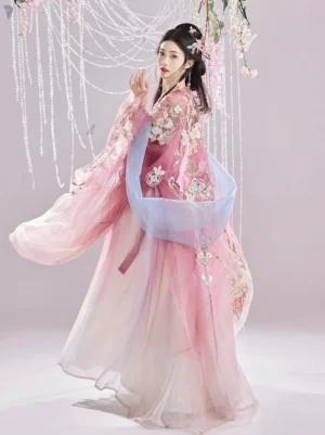 Front three quarter view of a pastel Tang Dynasty Hanfu Heziqun outfit with floral embroidery, flowing semi-sheer sleeves, gradient pink ivory skirt, and blue sash
