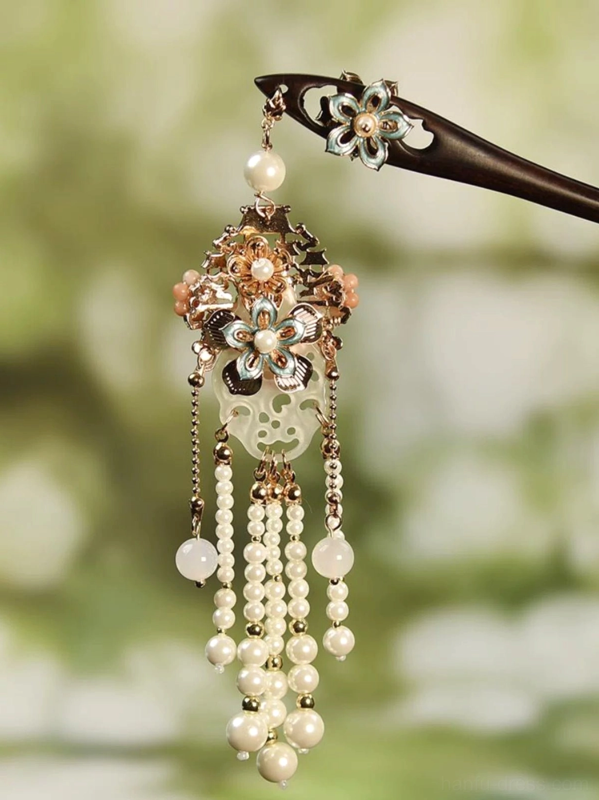 Traditional Chinese floral tassel hair stick with black wooden shaft, enamel flower ornament, pink flower pendant, carved jade-inspired charm, pearl tassels, and gold-tone chains against a soft green background