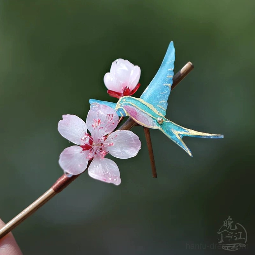 Close-up of a peach blossom Chinese hair stick showing a fully bloomed pink flower, blue swallow with gold trim, and brown gradient wooden pin base