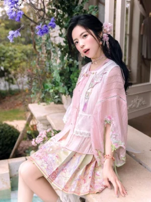 Layered Ming-style Hanfu with embroidered pink vest, sheer pleated top and floral mini horse face skirt photographed beside purple wisteria