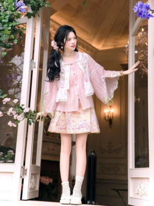 Modern Ming-style Hanfu outfit with sheer pink bell-sleeve top and floral mini mamianqun horse face skirt worn in a flower-filled doorway