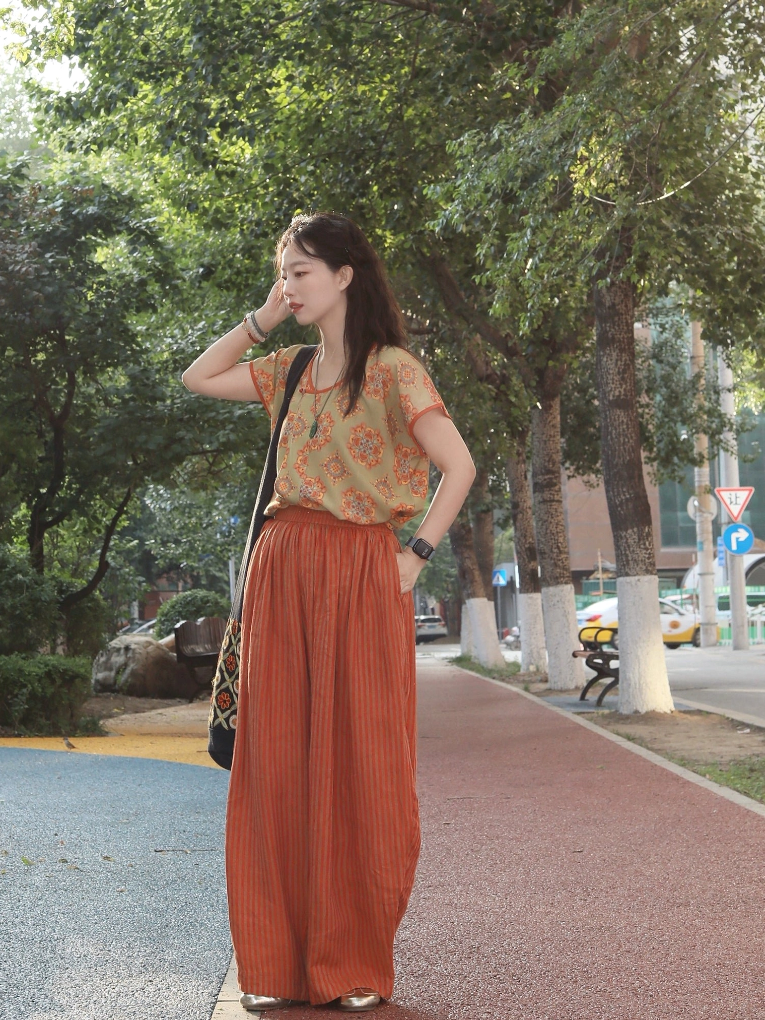 Full front view of a woman wearing a Peach Blossom modern Hanfu set with a vintage floral half-sleeve top and high-waisted rust-red linen pants styled with a wristwatch