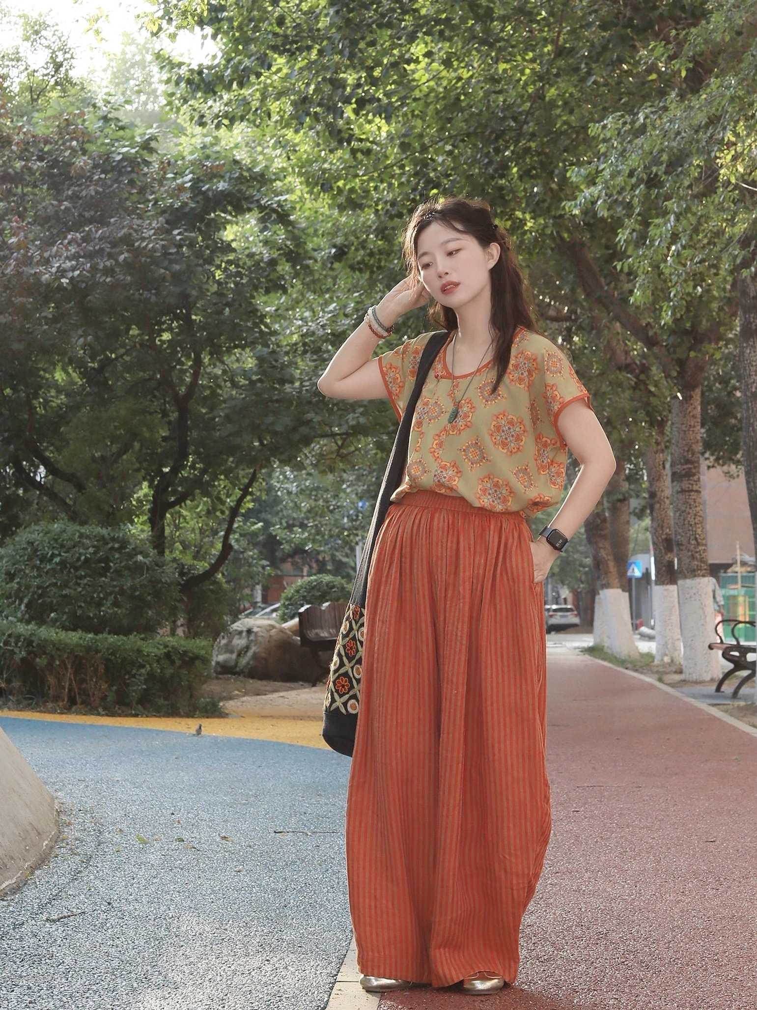 Front view of a woman wearing a Peach Blossom Tang-style modern Hanfu outfit with an olive-green floral half-sleeve top, rust-red trim, and high-waisted striped linen wide-leg pants