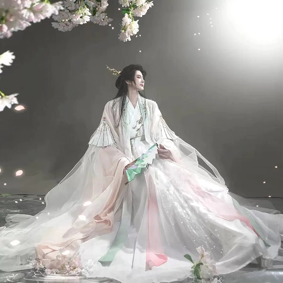 Full body side view of a unisex Peach Blossom Veil pink and white cross-collar Hanfu set with flowing floor length skirt sheer outer robe and traditional folding fan