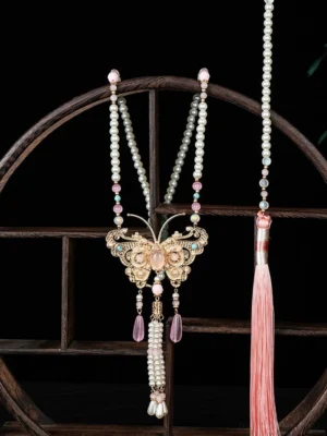Peach butterfly Chinese necklace with gold filigree pendant pearl chains pink crystal drops and long tassel displayed on a traditional wooden stand