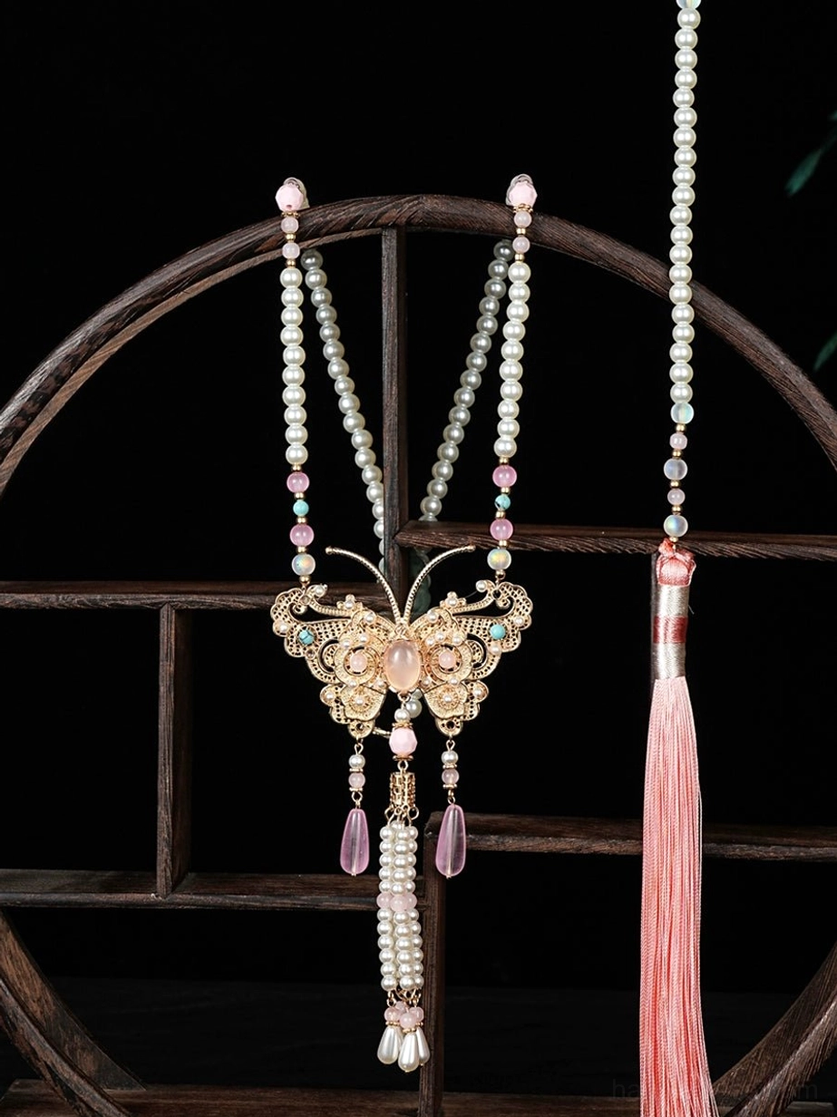 Peach butterfly Chinese necklace with gold filigree pendant pearl chains pink crystal drops and long tassel displayed on a traditional wooden stand
