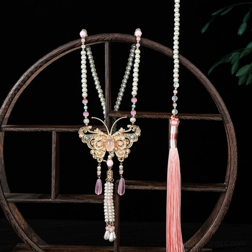 Peach butterfly Chinese yingluo necklace on a traditional wooden display with gold butterfly pendant pearl tassels pink teardrop charms and long pink tassel