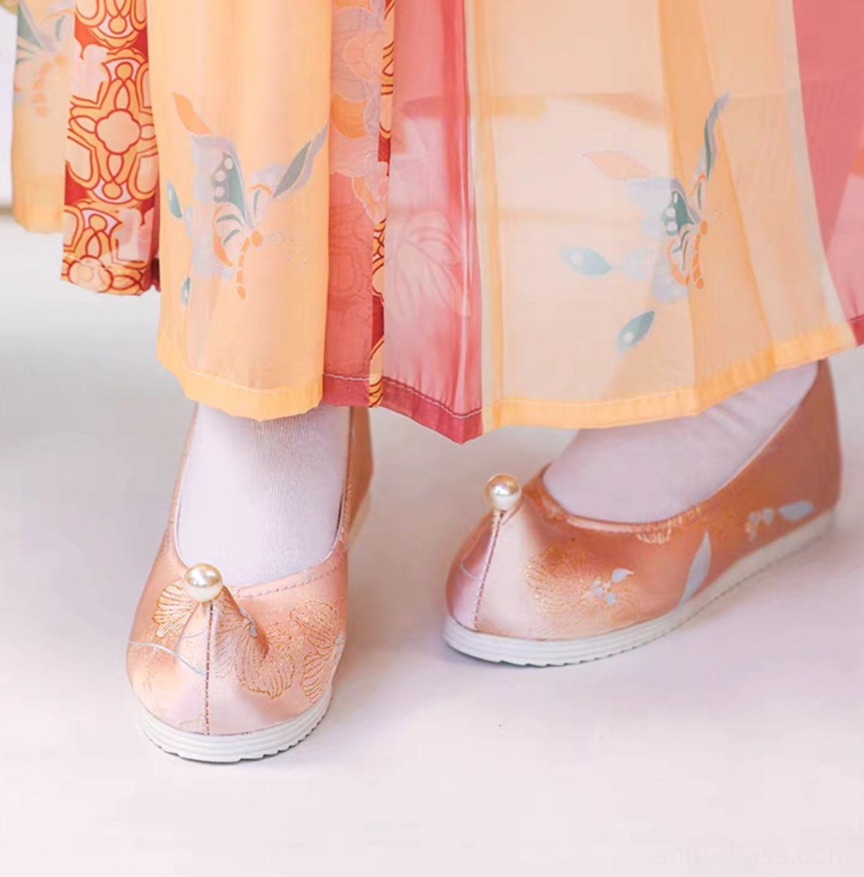 Peach pink embroidered Chinese Hanfu shoes with elegant upturned toes, pearl ornament, white rubber soles, and floral details worn with a traditional Hanfu skirt
