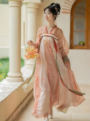 Three-quarter view of a peach pink Tang Dynasty Hanfu dress with high-waisted Qixiong Ruqun silhouette, sheer layered details, and red green ribbon accents
