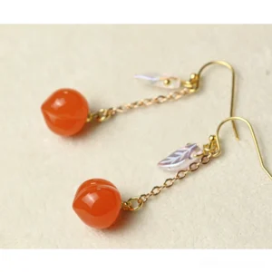 Flat lay of peach resin drop earrings with delicate gold chains, clear crystal-style ear hook details, peach charms, and iridescent leaf pendants