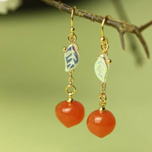 Peach resin drop Hanfu earrings hanging from a natural twig with gold-tone hooks, iridescent leaf charms, and reddish-orange peach beads