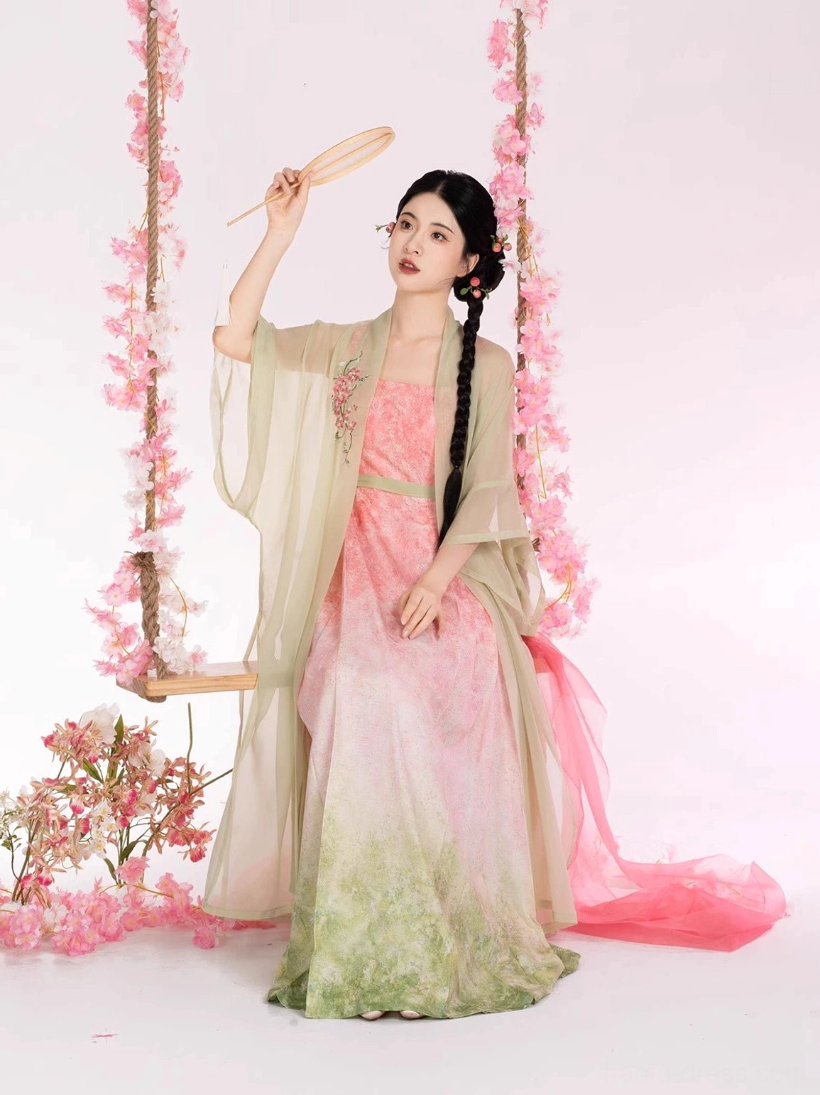 Woman in a Peach Willow Branch Hanfu two-piece set sitting on a flower swing with a sheer flowing beizi robe, floral embroidered dress, and traditional handheld fan