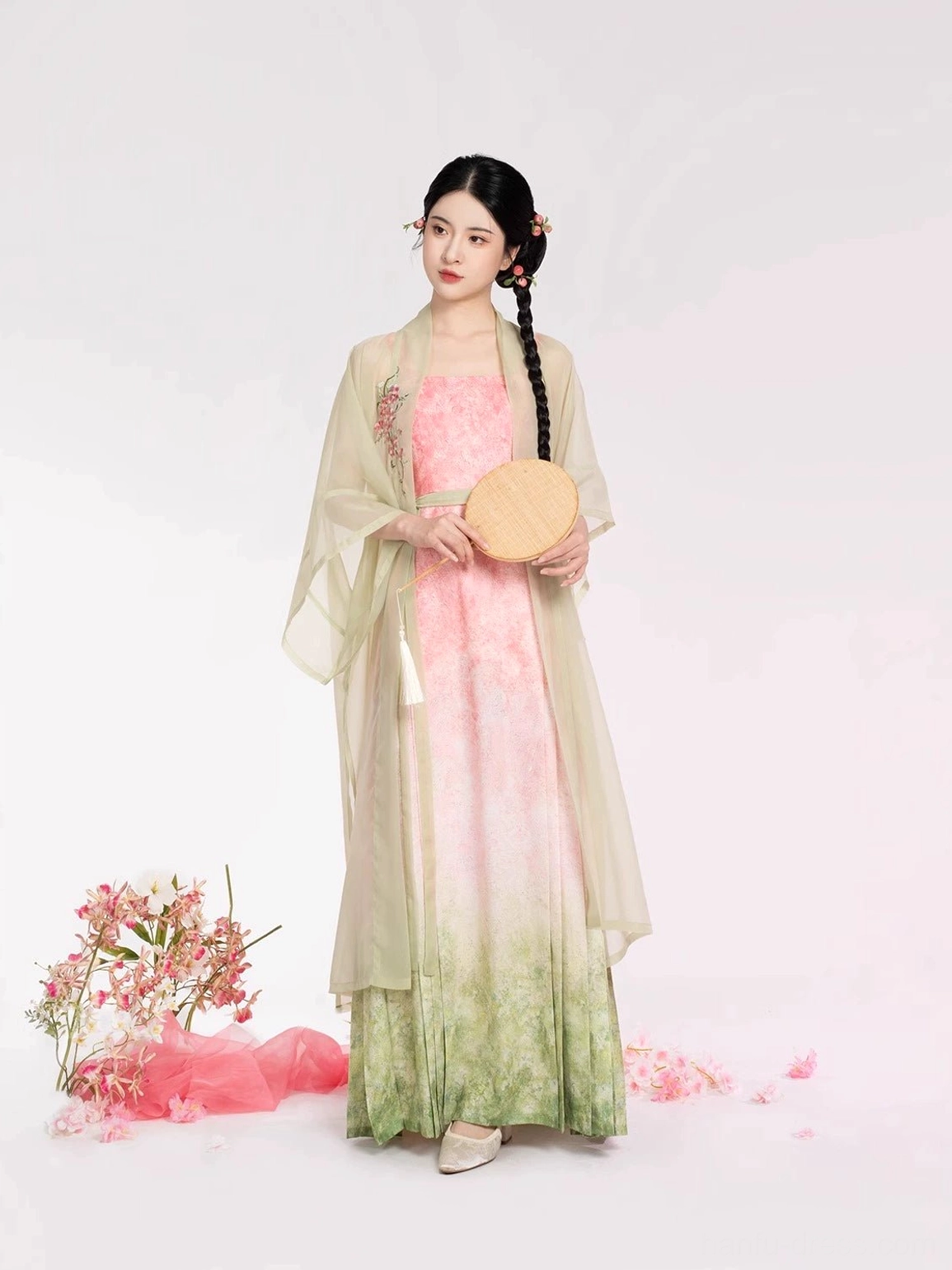 Three-quarter front view of Peach Willow Branch Song Dynasty Hanfu in pastel pink and sage green ombre colors with a round woven fan