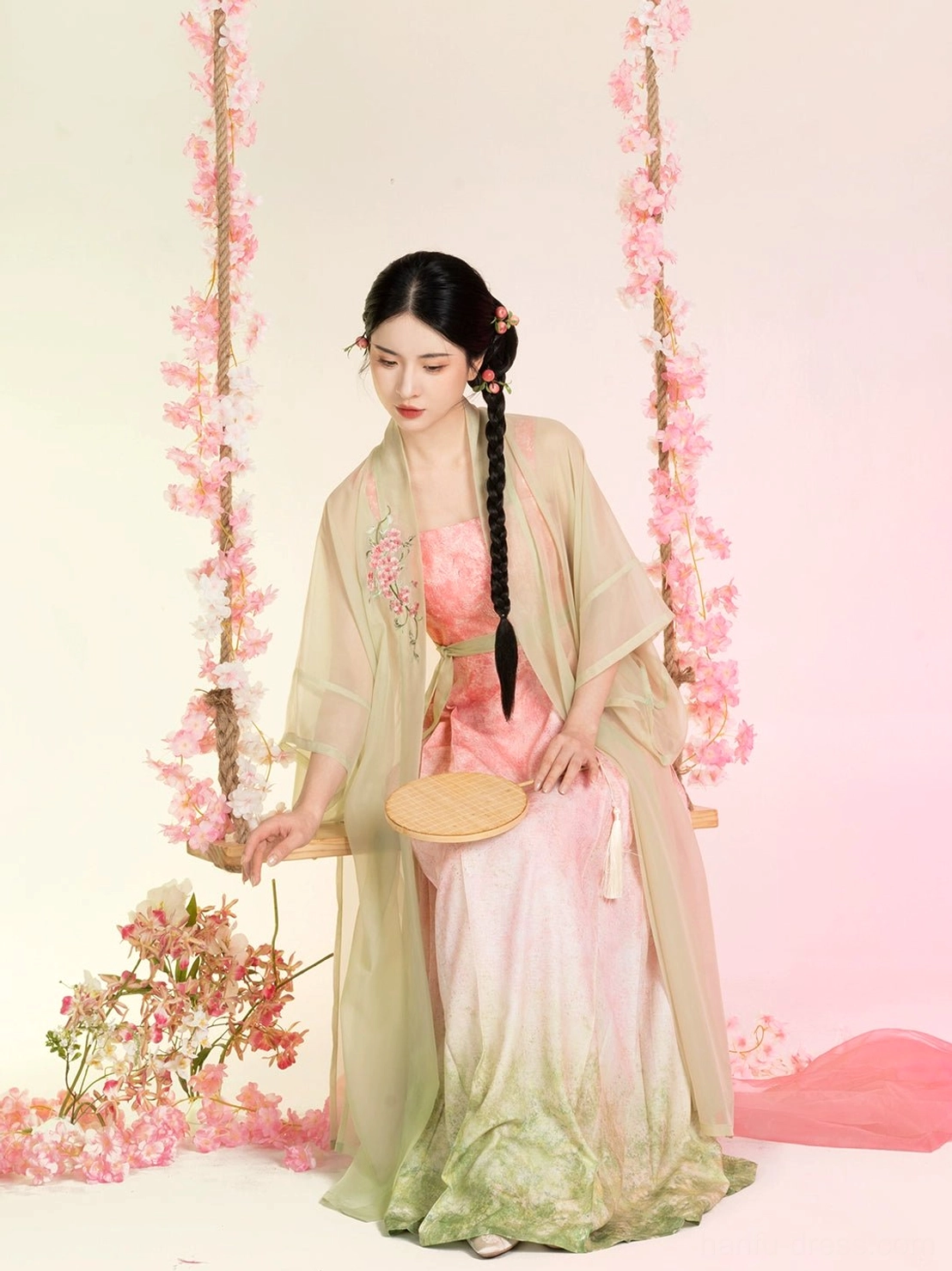 Three-quarter view of a woman wearing a Peach Willow Branch Song Dynasty Hanfu set with a sheer beizi jacket and pink-to-sage gradient mamian slip dress on a floral swing