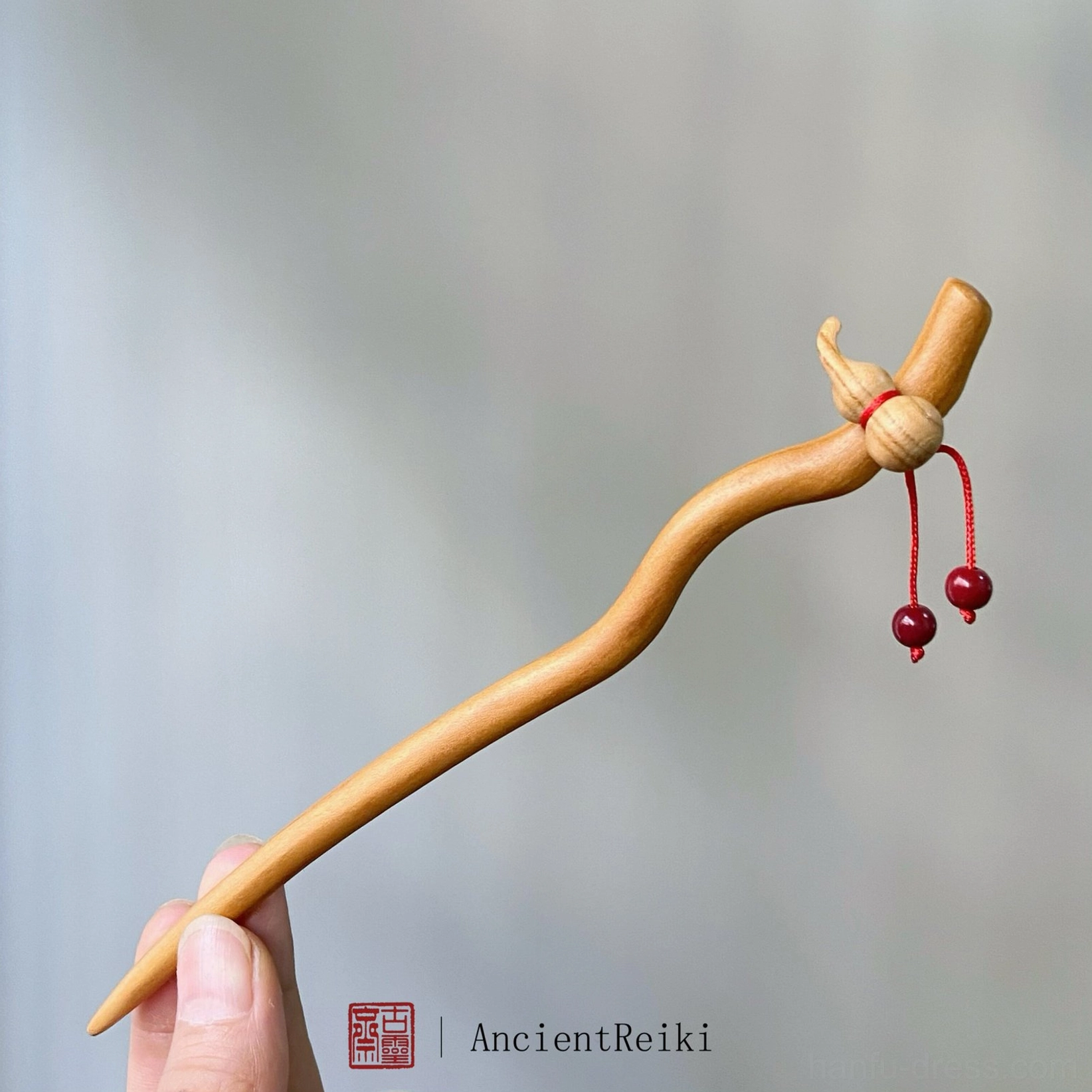Peach wood Chinese hair stick held in hand featuring a hulu gourd charm red cord and cinnabar bead pendants