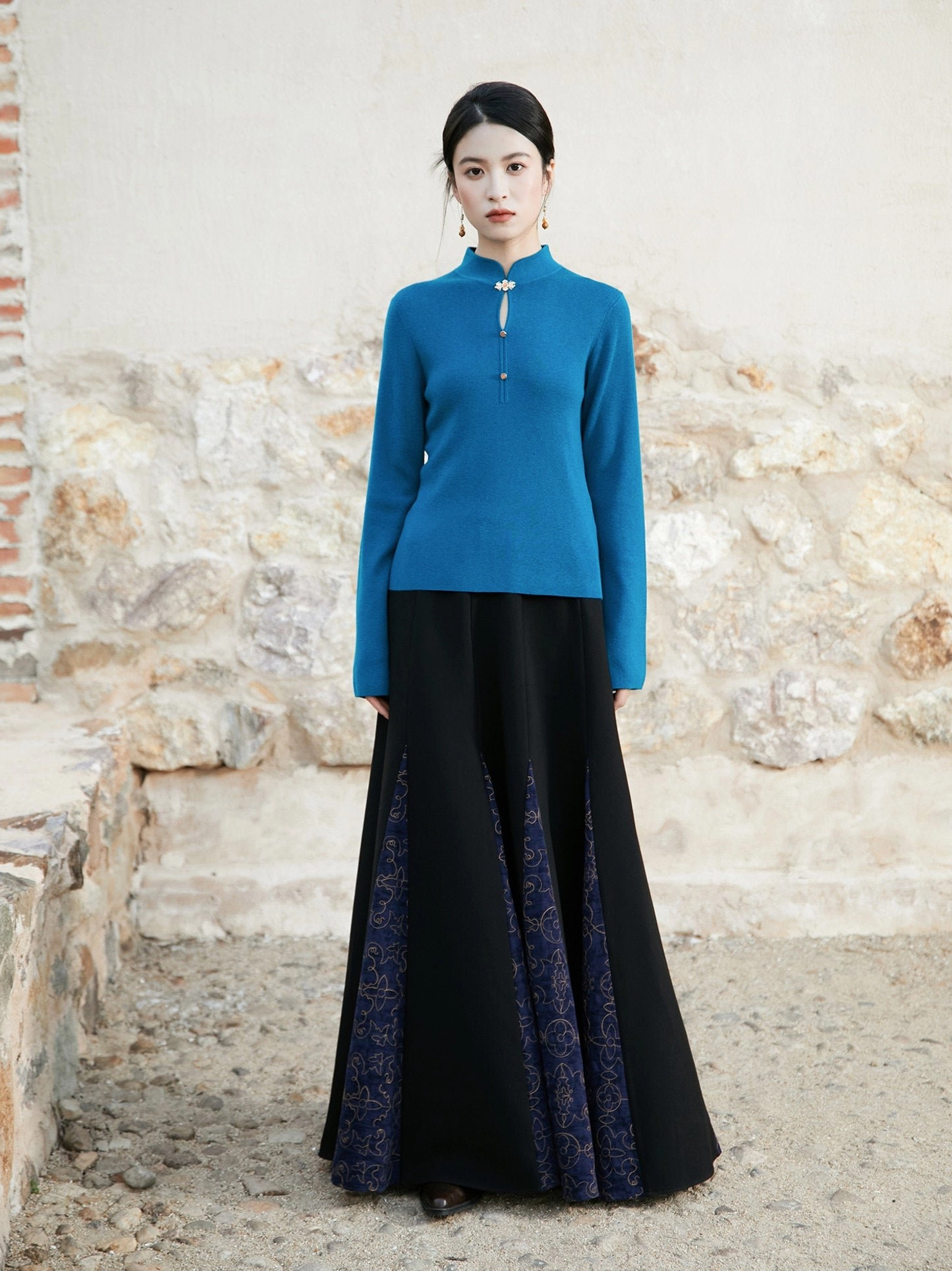 Full-body view of a peacock blue Chinese-style stand collar knitted sweater paired with a black long skirt and purple patterned side panels