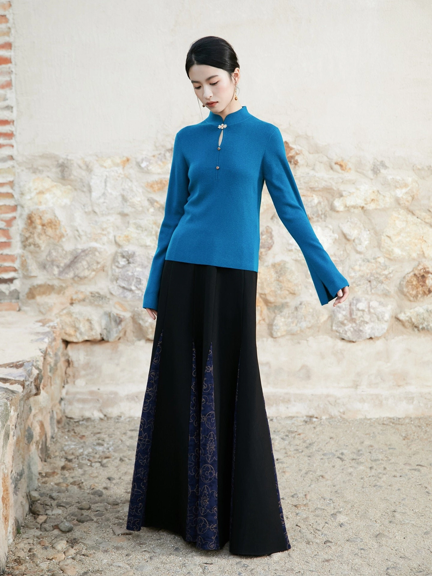 Side view of a woman wearing a peacock blue modern Hanfu knit top with a traditional mandarin collar and patterned long skirt