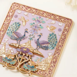 Peacock garden Chinese folding table mirror in a blush pink finish shown from an angled overhead view, with gilded floral borders, raised peacock artwork, birds, blossoms, mountains, clouds, and a foldable stand