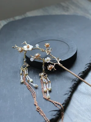 Pear blossom Chinese hair stick for Hanfu with white floral branch, gold-tone metal setting, pearl-like beads, and layered tassel chains on a dark stone tray