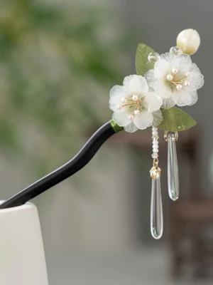 Pear blossom Chinese hair stick displayed on a white stand with white organza flowers, green leaves, pearl-like centers, and clear crystal tassels