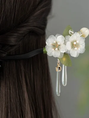 Pear blossom Chinese hair stick worn in a long dark half-up hairstyle, showing white floral ornament and dangling clear crystal tassels from the back