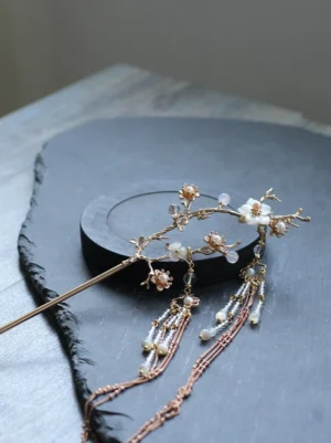 Side close-up of pear blossom Hanfu hair stick showing rose-gold-tone framework, dangling crystal-like beads, pearl-like drops, and fine chain tassels