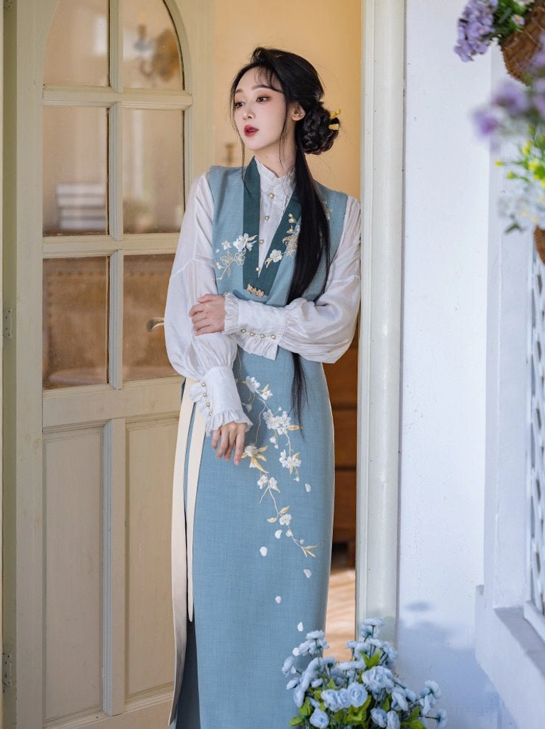 Three-quarter view of a Pear Blossoms Song Dynasty Hanfu three-piece outfit with white lantern sleeve shirt, light blue embroidered vest, two-tone wrap skirt, and dark green trim