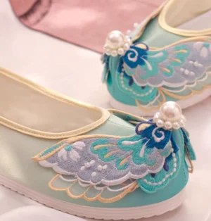 Close-up of traditional Chinese Hanfu shoe with blue purple and gold embroidery pearl cluster decoration upturned toe and cream trim