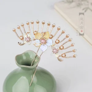 Close-up of a vintage fan-shaped Chinese hairpin with gold-toned metal, iridescent flower ornaments, and pearl accents displayed on a green porcelain vase