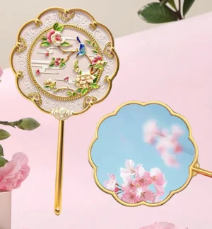 Peony and bluebird Chinese hand mirror with scalloped floral frame, gold-tone handle, enamel-style garden artwork, and clear mirror surface