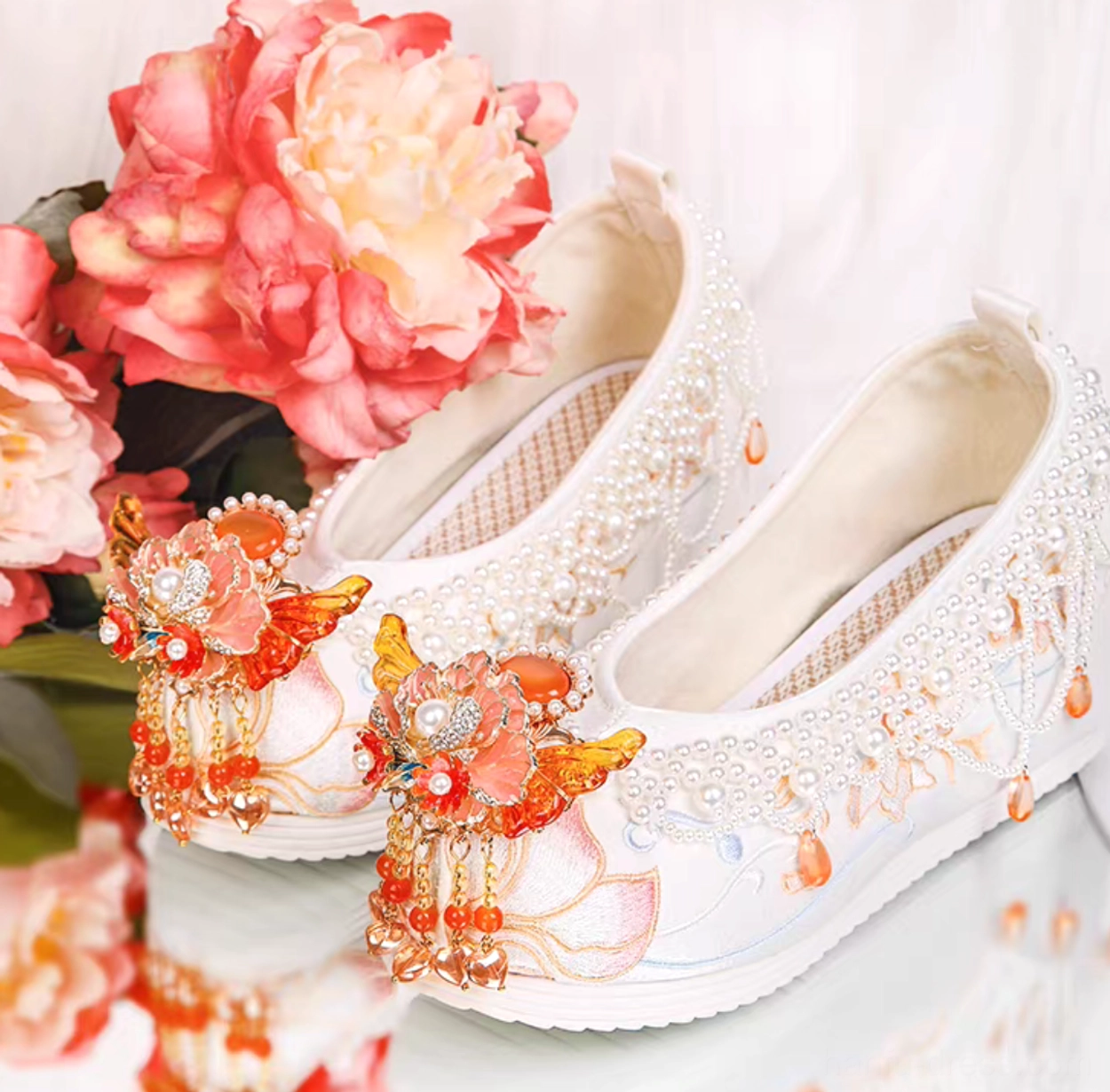 White traditional Chinese Hanfu shoes with peony-inspired flower tassels, pearl trim, and lotus embroidery shown in a three-quarter side view with peony flowers