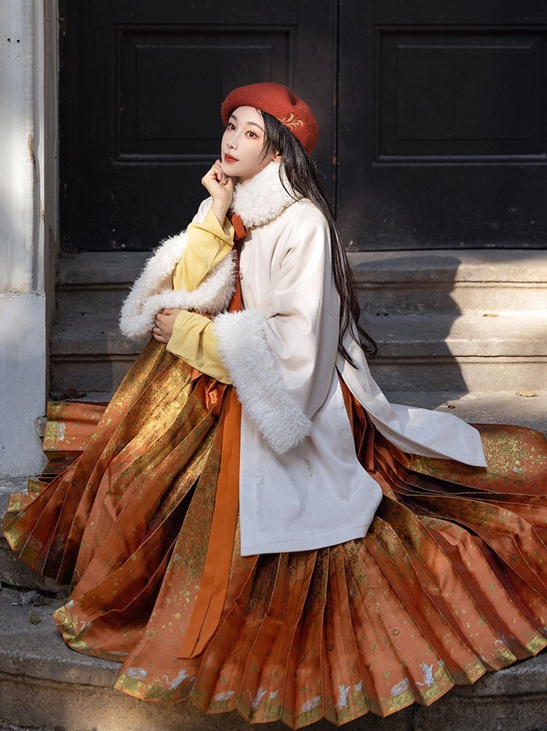 Seated model wearing persimmon embroidered Ming Dynasty Hanfu coat with flowing orange Mamianqun skirt