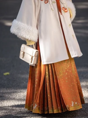 Close-up side view of ivory faux fur trimmed Hanfu coat and orange gold brocade Mamianqun skirt