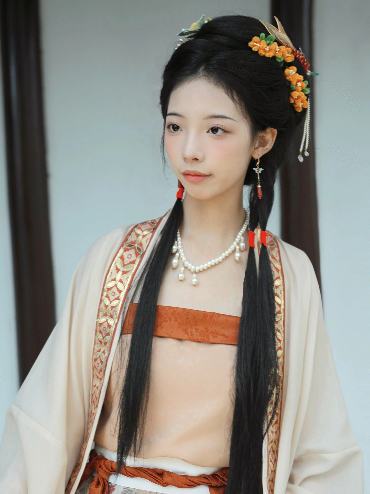 Upper-body close-up of a persimmon-inspired Song Dynasty Hanfu with gold-trimmed cream beizi collar, terracotta waist band, pearl drop necklace, and traditional orange flower hairpins