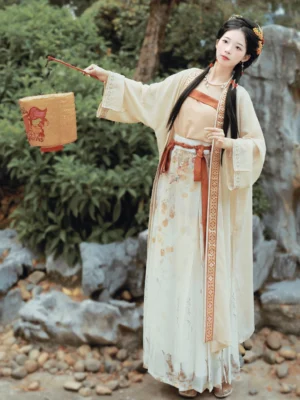 Front view of a persimmon-themed Song Dynasty Qiyao Ruqun Hanfu set with cream beizi coat, apricot camisole, printed wrap skirt, terracotta sash, and decorative paper lantern in a traditional Chinese rock garden