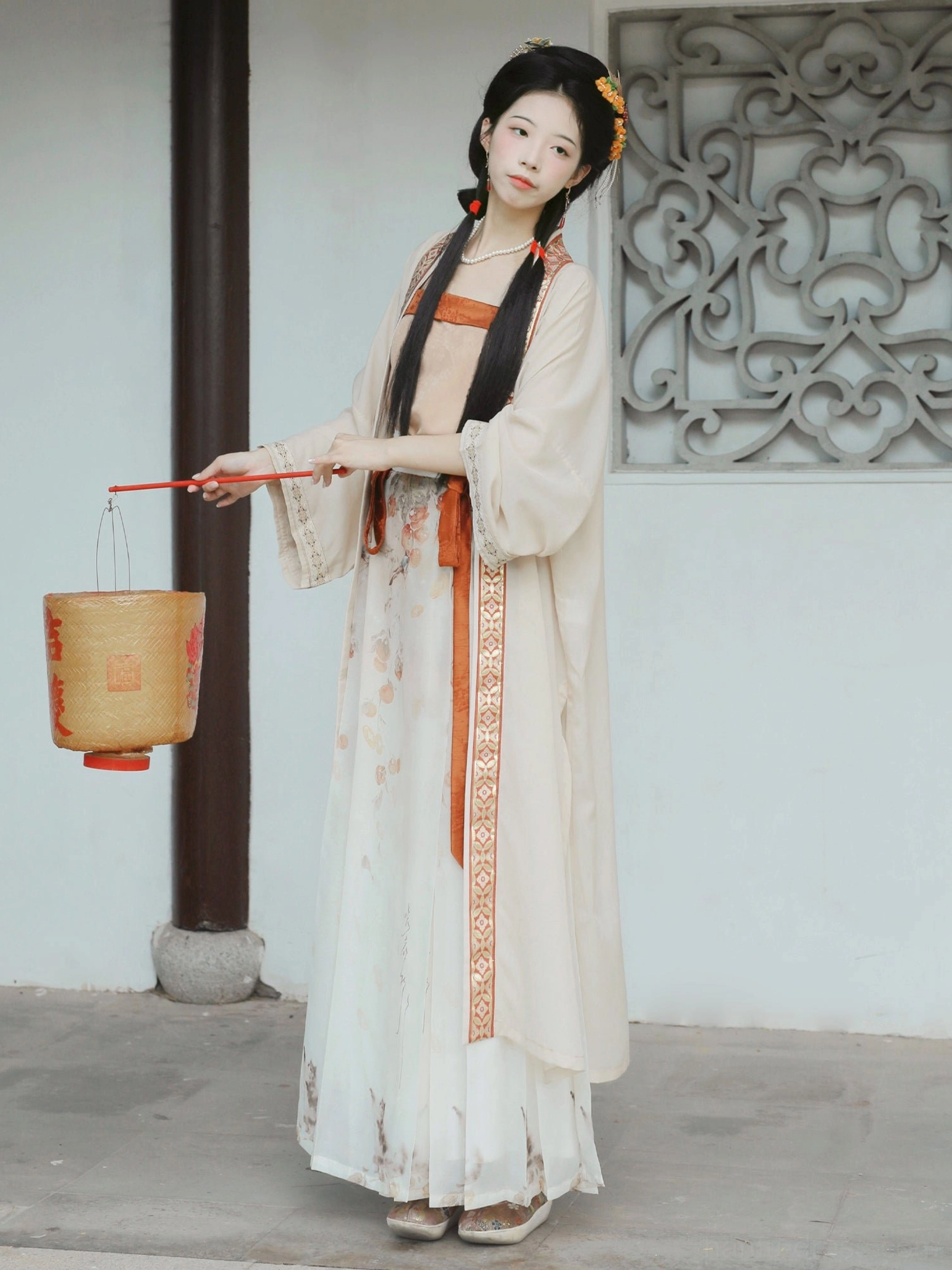 Side-front full view of the complete persimmon-themed Song Dynasty Qiyao Ruqun Hanfu with flowing cream outer robe, printed high-waisted skirt, terracotta sash, and coordinating accessories beside a carved wooden window